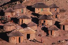 an aerial view of some huts with thatched roofs and people standing in the doorways