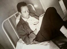 black and white photograph of a man sitting on a bed holding a cell phone to his ear