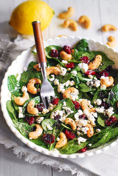 spinach salad with cashews, cranberries and feta cheese in a white bowl