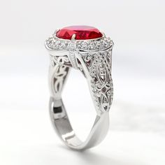 a fancy ring with a red stone surrounded by white diamonds and filigrees