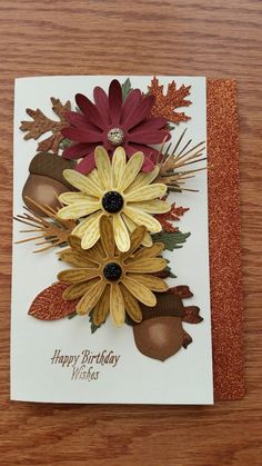 a happy birthday card with flowers and leaves on the front, sitting on a wooden table