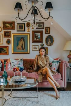 a woman sitting on top of a pink couch in front of a wall filled with pictures