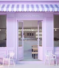 the entrance to a store with white chairs and tables in front of purple walls,