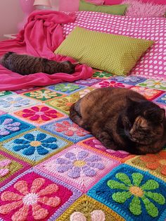 a cat laying on top of a bed covered in colorful crocheted blankets and pillows