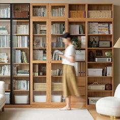 a woman walking through a living room with bookshelves in the background and a white rug on the floor