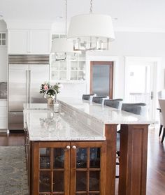 a kitchen with white cabinets and marble counter tops, an island in the middle is surrounded by wood flooring