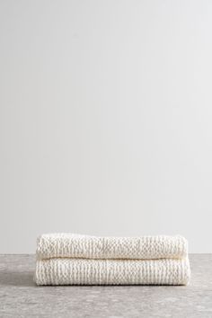 two white towels folded on top of each other in front of a gray wall and floor