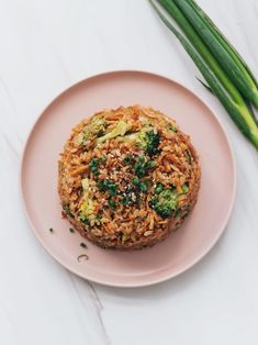 a pink plate topped with rice and broccoli on top of a white table