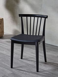 a black chair sitting on top of a hard wood floor next to a wooden vase