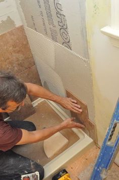 a man is working on the floor in front of a shower with tile and tools