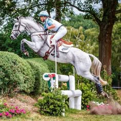 a man riding on the back of a white horse over an obstacle in a park