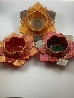 three glass flowers sitting on top of a white table next to an empty cup and saucer