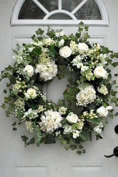 a wreath with white flowers and greenery hangs on the front door of a house