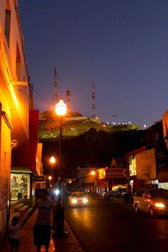 people walking down the street at night with cars parked on the side of the road