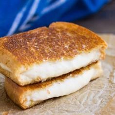 two grilled cheese sandwiches sitting on top of wax paper with a blue bag in the background