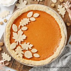 a pumpkin pie with leaves and nuts on a wooden board next to other autumn decorations