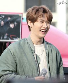 a young man holding a microphone in front of a pink car and smiling at the camera