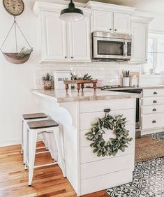 a kitchen with white cabinets and an island in the middle, surrounded by wreaths