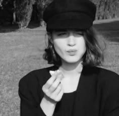 a black and white photo of a woman in a hat holding something up to her mouth