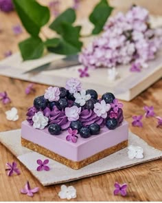 a piece of cake with blueberries and purple flowers on it sitting on a table