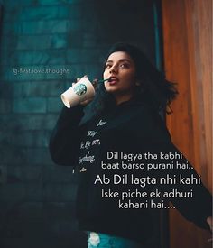 a woman drinking from a coffee cup while standing in front of a brick wall with words written on it