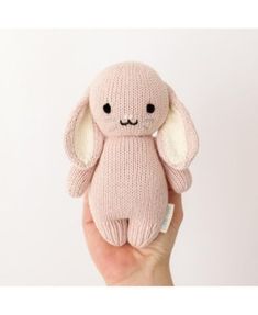 a hand holding a pink stuffed animal with ears on it's face and eyes closed