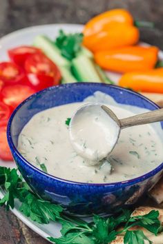 a blue bowl filled with white sauce sitting on top of a plate next to vegetables