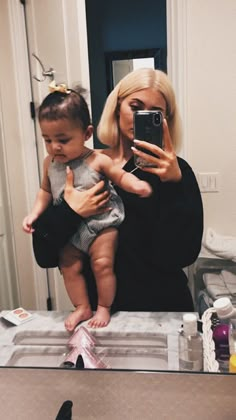 a woman holding a baby in front of a mirror taking a selfie with her cell phone