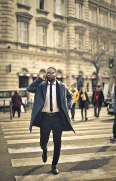 a man is walking across the street talking on his cell phone while wearing a suit and tie