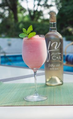 a pink drink sitting on top of a table next to a bottle