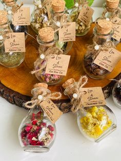 small glass bottles filled with different types of flowers and herbs on a wooden platter