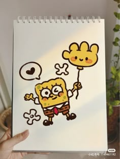 a hand holding up a notebook with an image of spongebob