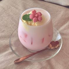 a dessert in a glass dish on a plate with a spoon and flower decoration next to it