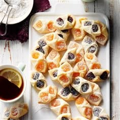 small pastries with oranges and blackberries are on a plate next to a cup of tea