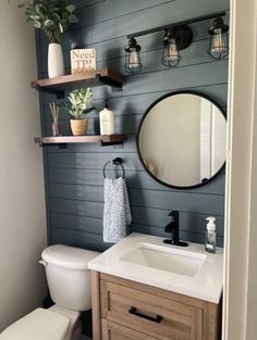 a white toilet sitting under a bathroom mirror next to a wooden sink vanity and shelf