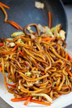 stir fried noodles with carrots and other vegetables in a wok on the table