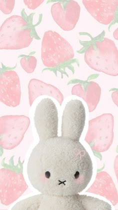 a white stuffed animal sitting in front of a pink background with strawberries on it