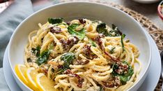 a white bowl filled with pasta and spinach on top of a table next to lemon wedges