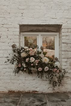 a window that has some flowers on the side of it and is next to a brick wall