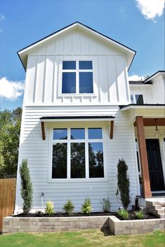 a white house with black doors and windows on the front porch, grass in front of it