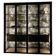 an empty glass display case in front of a white wall with black and grey designs