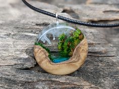 a wooden necklace with a glass pendant hanging from it's side on a piece of wood