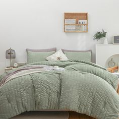 a bed with green comforter and pillows in a room next to a white wall