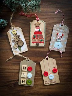 four tags with buttons and christmas decorations hanging from them on a wooden table next to a tree