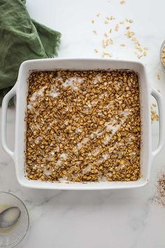 a white casserole dish filled with oatmeal next to two spoons