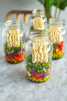 four mason jars filled with noodles and veggies on top of a marble counter