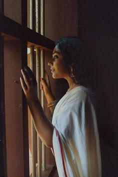 a woman is looking out the window with her hand on the bars in front of her