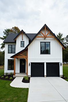 a white house with black garage doors and two large windows on the front of it