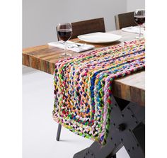 a table topped with a colorful crocheted blanket next to a plate and glass of wine