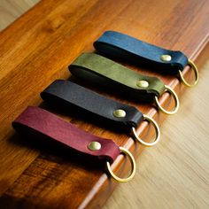 four different colored leather keychains on a wooden surface with gold rings and metal clasps